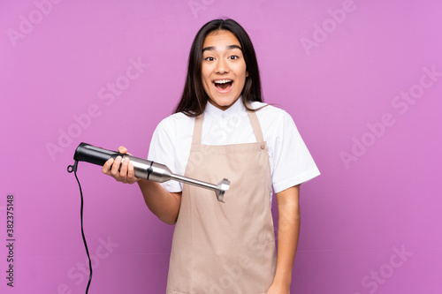 Indian woman using hand blender isolated on purple background with surprise facial expression