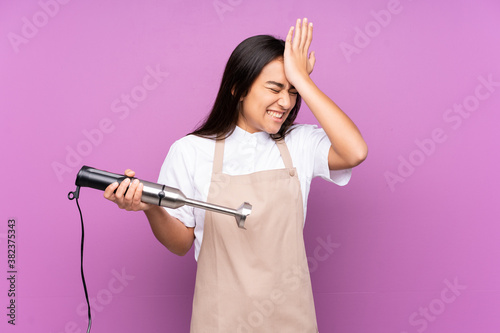 Indian woman using hand blender isolated on purple background having doubts with confuse face expression