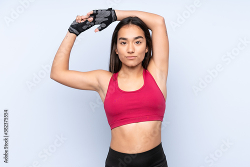 Young Indian sport woman isolated on blue background stretching