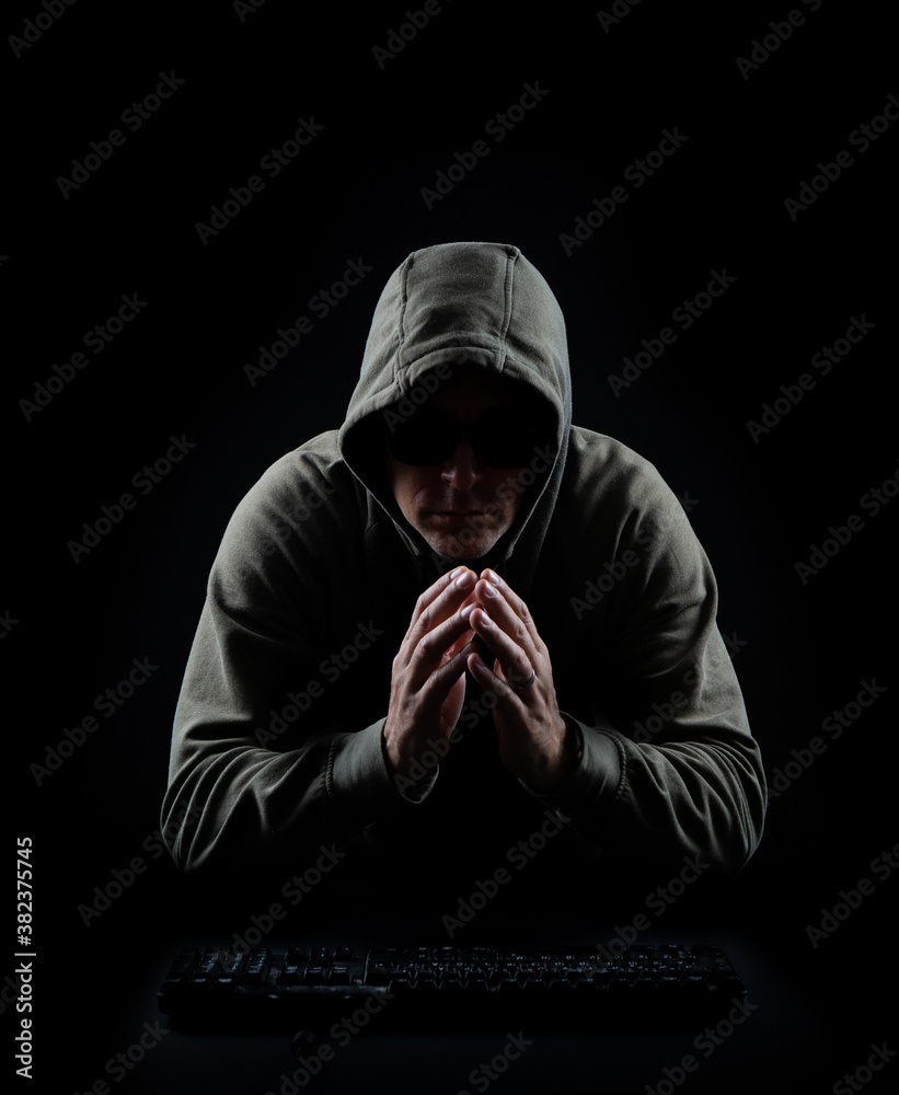 Dark hacker with hooded sweatshirt in front of keyboard in a black and low key setting