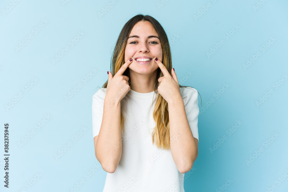 Young caucasian woman isolated on blue background smiles, pointing fingers at mouth. Young caucasian woman isolated on blue background smiles, pointing fingers at mouth.