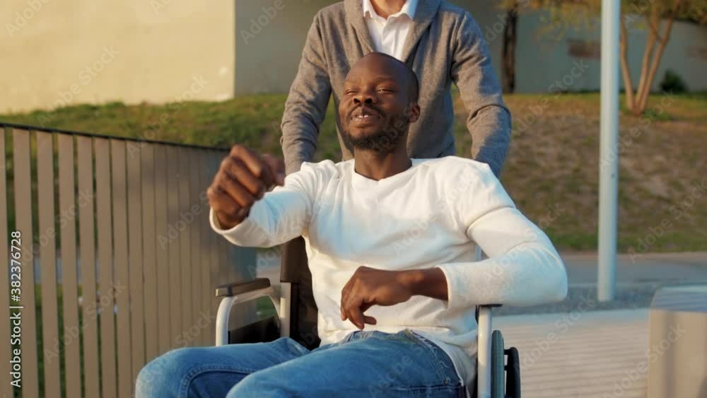 Young african american man have fun imagines driving car on a wheelchair ride with friend in autumn park. Support attractive walking transportation health medical together. Slow motion