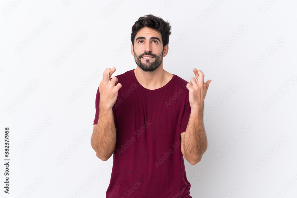 Fototapeta premium Young handsome man with beard over isolated white background with fingers crossing and wishing the best
