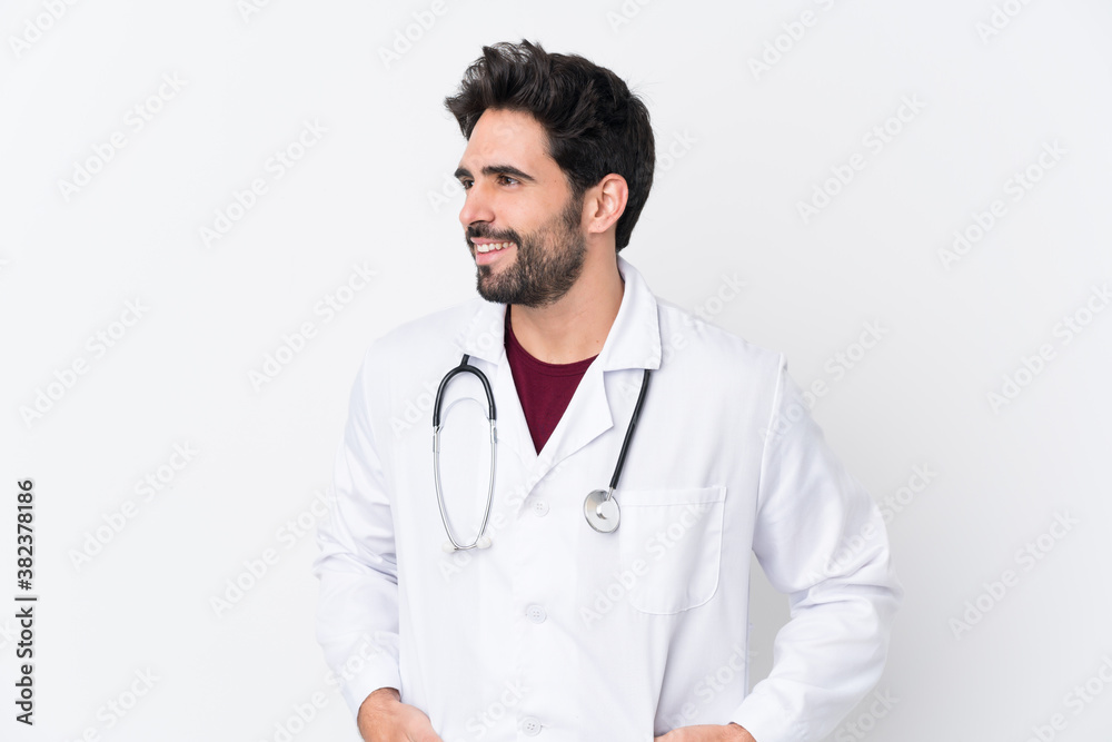 Young handsome man with beard over isolated white background wearing a doctor gown and with stethoscope Young handsome man with beard over isolated white background wearing a doctor gown and with stethoscope