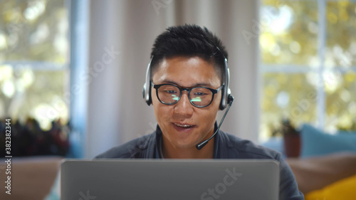 Young asian businessman working on laptop in headset having video conference at home