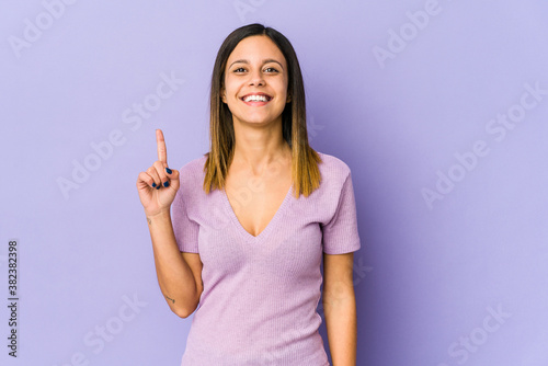 Young woman isolated on purple background showing number one with finger. © Asier