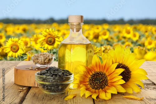 Sunflower oil and seeds on wooden table near blooming field