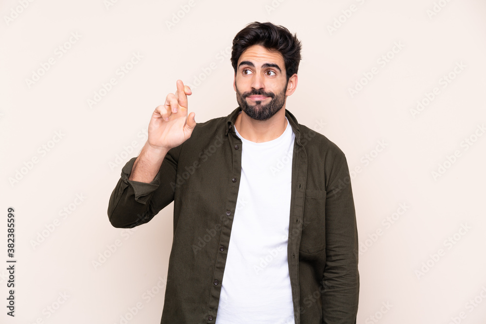 Young handsome man with beard over isolated background with fingers crossing and wishing the best Young handsome man with beard over isolated background with fingers crossing and wishing the best
