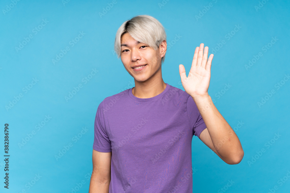 Fototapeta premium Young asian man over isolated blue background saluting with hand with happy expression