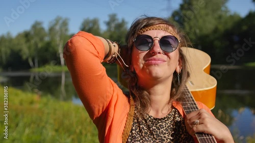 nature, summer vacation, vacation and people concept - happy smiling woman in sunglasses stands with a guitar on her shoulder. photo