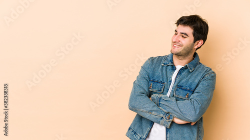 Young man isolated on beige background smiling confident with crossed arms. © Asier