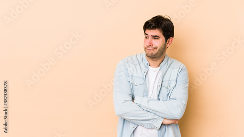 Young man isolated on beige background confused, feels doubtful and unsure.