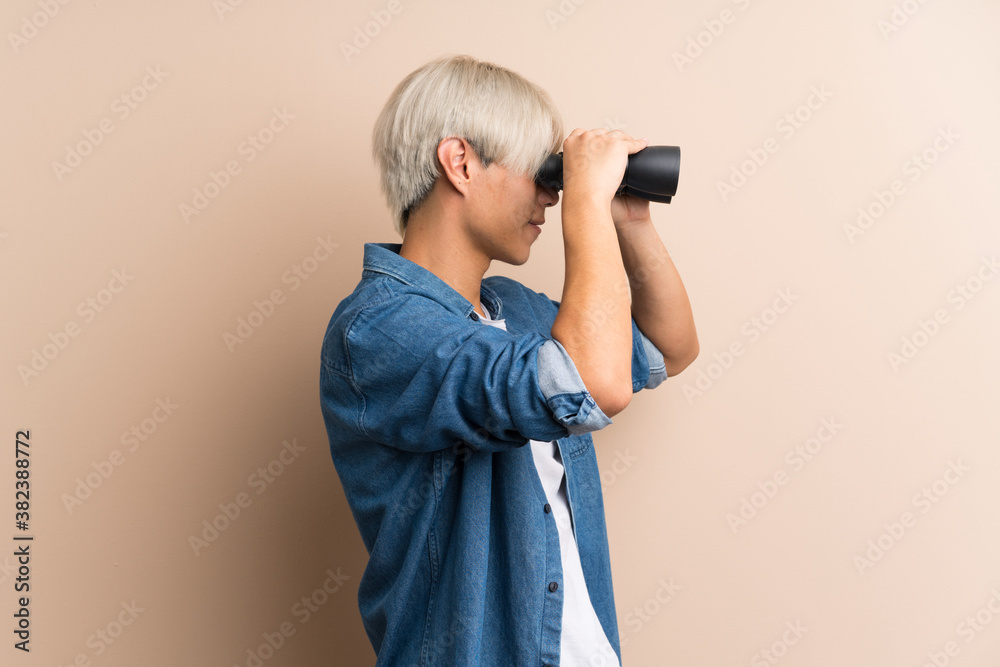 Obraz premium Young asian man over isolated background with black binoculars
