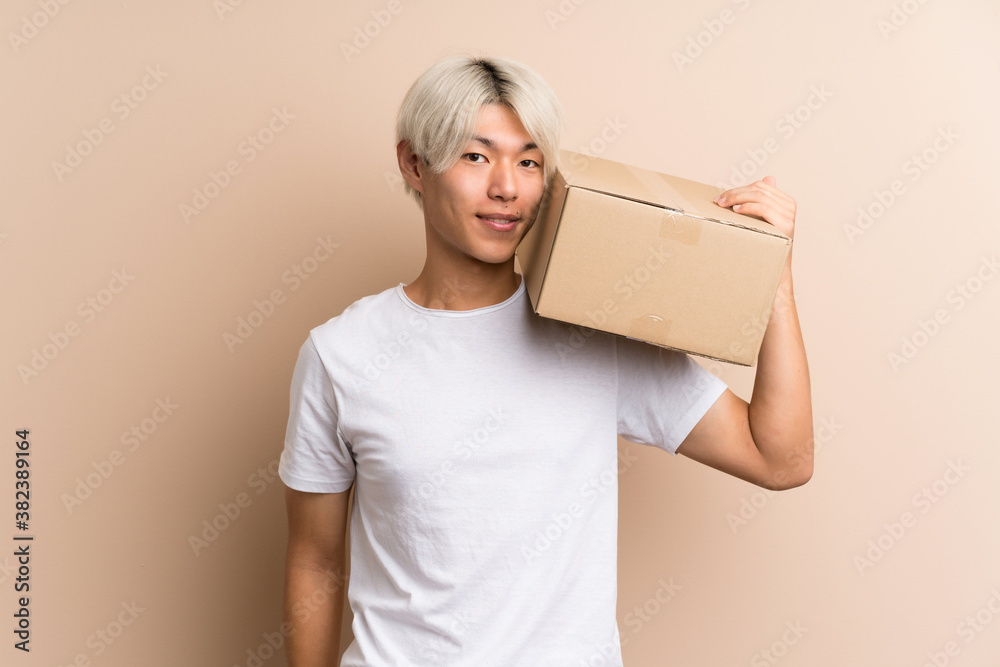 Young asian man over isolated background holding a box to move it to another site Young asian man over isolated background holding a box to move it to another site