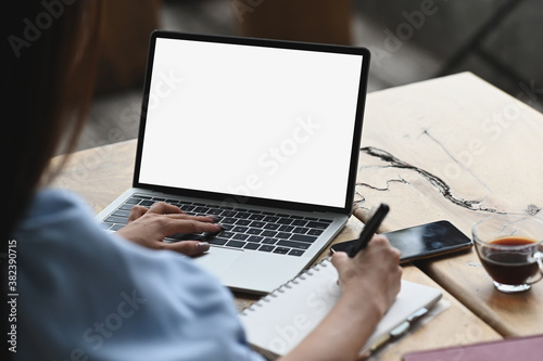 Cropped shot of young woman working on laptop with white screen on wooden table.
