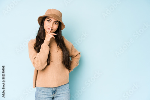 Young indian woman wearing a hat isolated on blue background thinking and looking up, being reflective, contemplating, having a fantasy.
