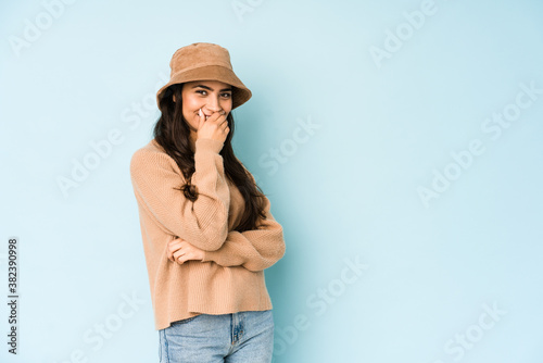 Young indian woman wearing a hat isolated on blue background laughing happy, carefree, natural emotion.