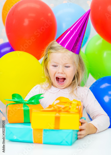 Surprised little girl wearing party's cap holds many gift boxes