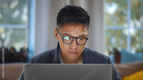 Close up of young asian man in glasses working on laptop at home office