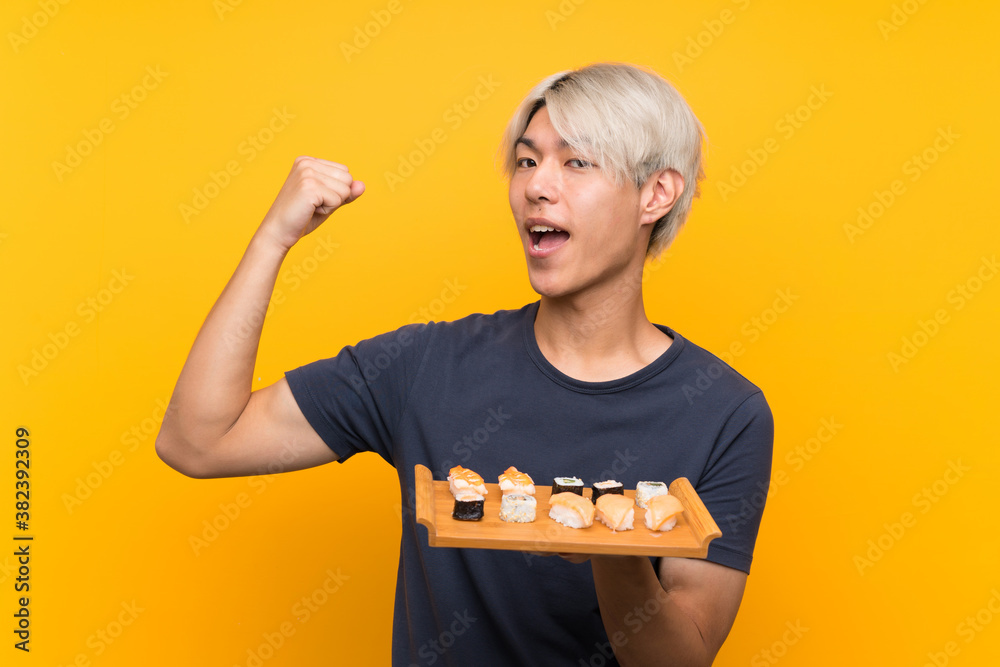 Young asian man with sushi over isolated yellow background making strong gesture Young asian man with sushi over isolated yellow background making strong gesture