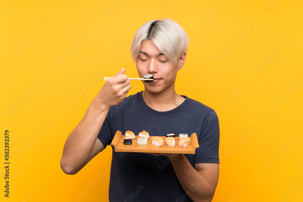 Young asian man with sushi over isolated yellow background Young asian man with sushi over isolated yellow background
