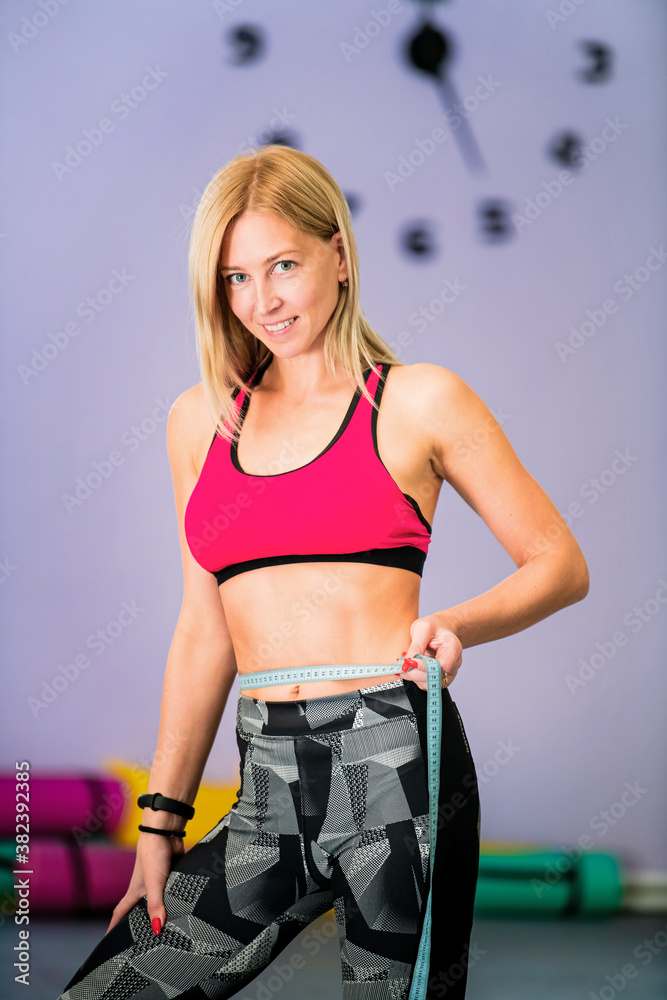 beautiful sportive woman works out in the gym, measures her waist with centimeter beautiful sportive woman works out in the gym, measures her waist with centimeter
