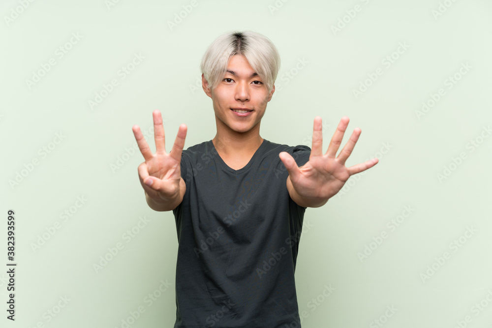 Young asian man over isolated green background counting eight with fingers Young asian man over isolated green background counting eight with fingers