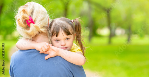 Woman holds in her arms a sad daughter with down syndrome. Empty space for text