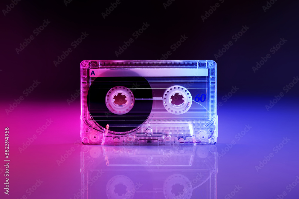 Retro audio cassette tape lit by pink and blue lamps on a black background with reflection