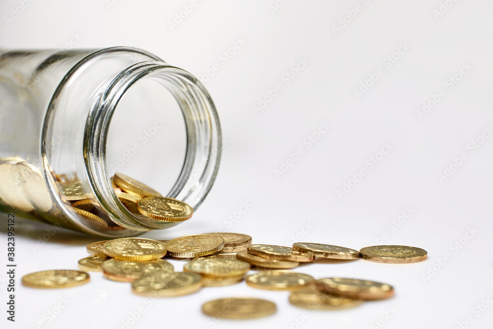 Collection of coins spilling out of a glass jar tipped on its side Collection of coins spilling out of a glass jar tipped on its side