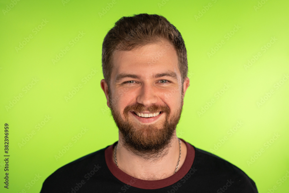 Funny bearded man broadly smiles on green background. Studio portrait of young happy Man looking at camera. Positive Male Caucasian model on chromakey background. High quality photo.