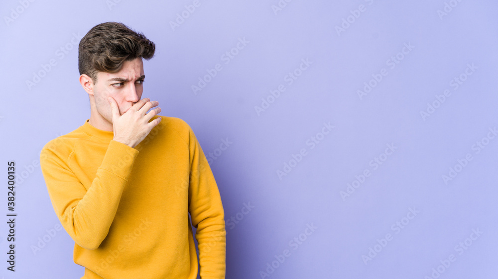 Young caucasian man isolated on purple background thoughtful looking to a copy space covering mouth with hand. Young caucasian man isolated on purple background thoughtful looking to a copy space covering mouth with hand.