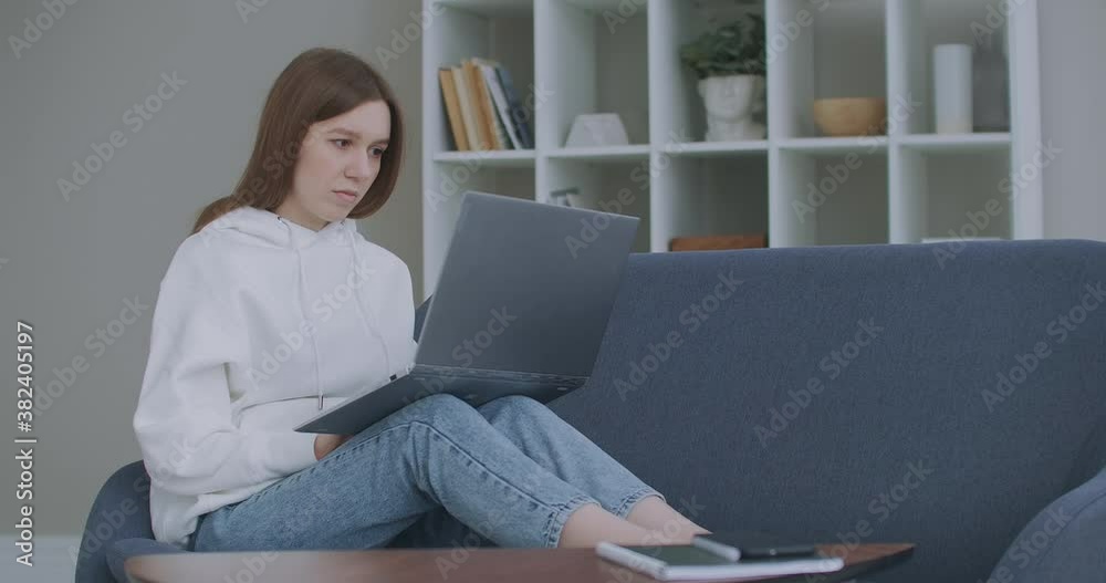 Woman using laptop on couch at home. Thoughtful young woman sitting with computer on couch, looking outside, concentrate on work, feeling bored, need additional motivation, working remotely at home. Woman using laptop on couch at home. Thoughtful young woman sitting with computer on couch, looking outside, concentrate on work, feeling bored, need additional motivation, working remotely at home.