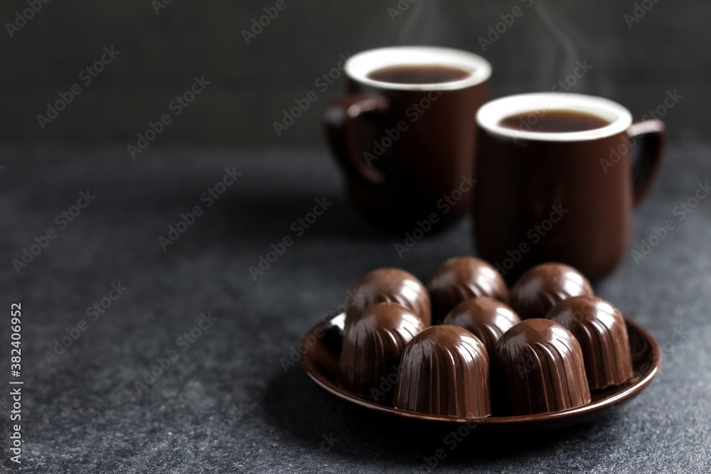Chocolate candies on a plate and two cups of coffee on black background Chocolate candies on a plate and two cups of coffee on black background