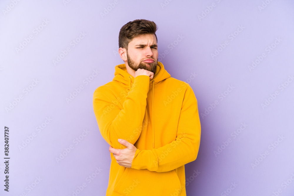 Young man isolated on purple background suspicious, uncertain, examining you. Young man isolated on purple background suspicious, uncertain, examining you.