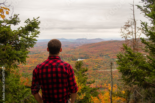 Back view of a man with a lumberjack shirt admiring the autumnal view in the Mont-Orford national park, Canada photo