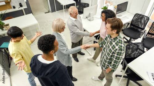 Cheerful young team greeting new employees, Aged man and woman, senior interns shaking hands with colleagues in the modern office