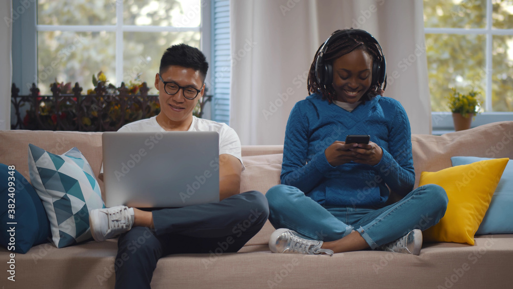 Obraz premium Happy multiracial couple with modern gadgets networking or messaging at home