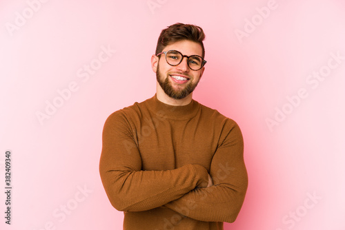 Young caucasian man isolated on pink background who feels confident, crossing arms with determination. © Asier