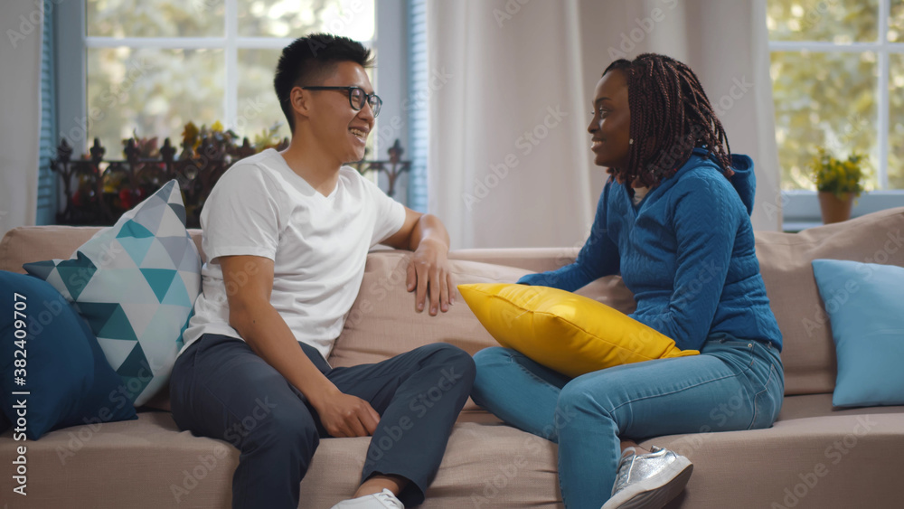 Nice multiethnic couple communicating and sitting on sofa at home Nice multiethnic couple communicating and sitting on sofa at home