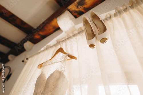 The bride's wedding dress on a hanger and white shoes on the background of closed curtains on the cornice.