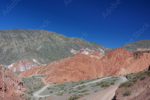 A dirt road winds through colorful mountains behind the town of Purmamarca, Humahuaca Valley, northern Argentina