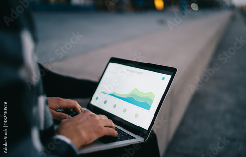 Cropped image of man's hands typing on laptop computer keyboard making online research browsing web pages, skilled male checking graphic charts in social media using technology outdoors and 4G