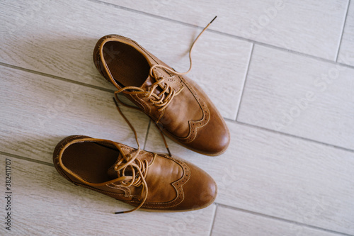 Brown men's shoes with untied laces on a white laminate.