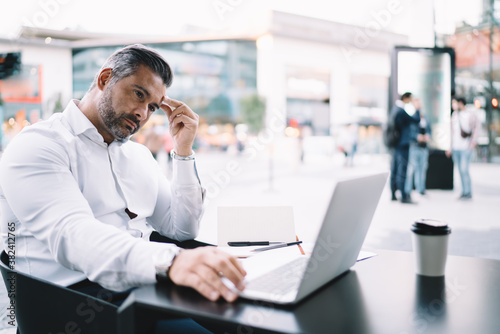 Middle aged businessman watching received video message pondering on strategy information during distance job in sidewalk, thoughtful male employee reading financial publication analyzing trade