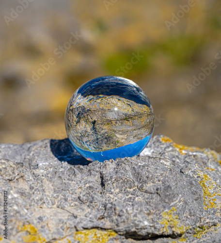 Photography Crystal Photo Ball showing upside down reflection of sky beach and waves balanced on rocks on sandy beach.