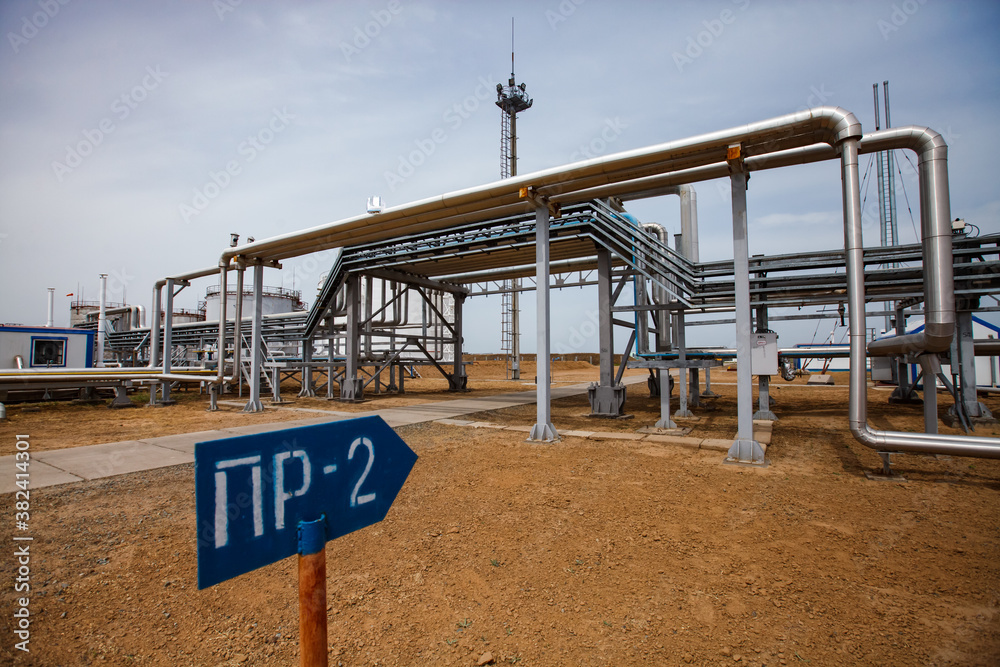 Oil refinery and gas processing plant. Pipelines and lighting mast and sign on desert background and blue sky.