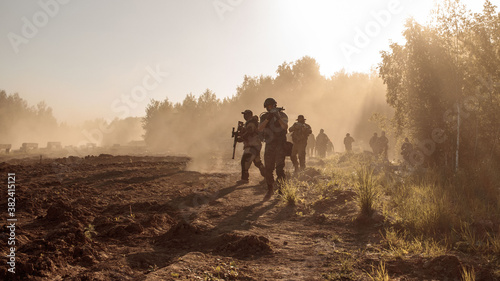 A group of soldiers goes through the field along the forest in the smoke. photo