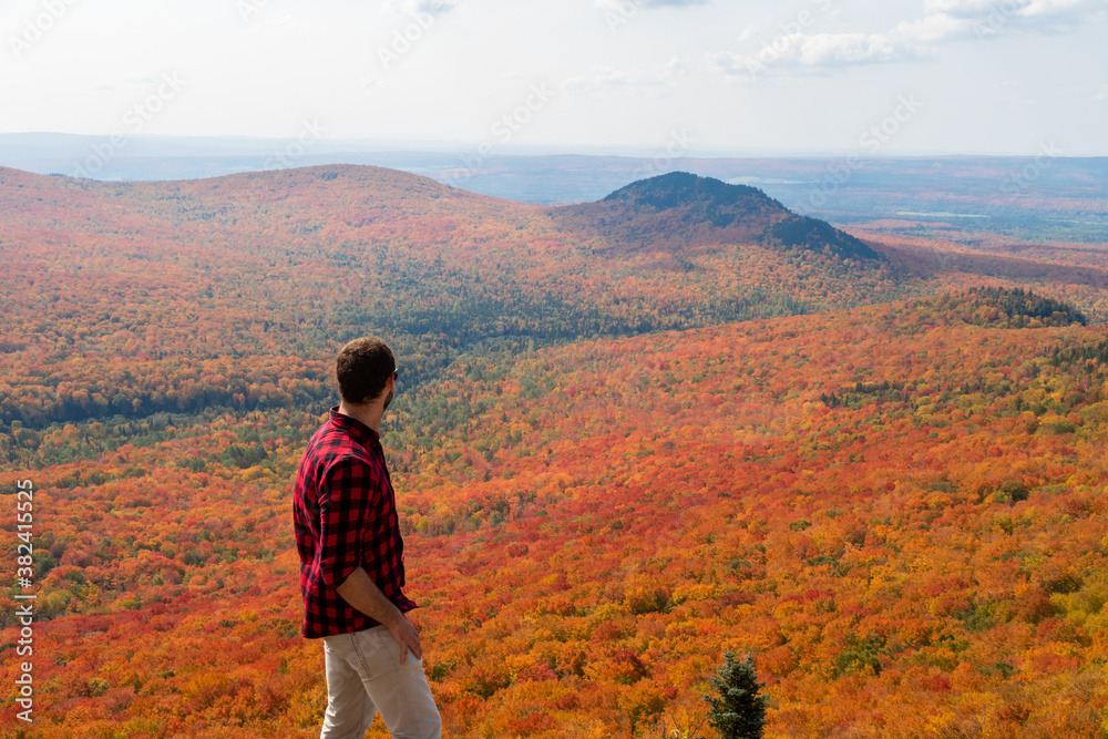 Young man with a lumberjack shirt, admiring the automnal view in the Megantic national park, Canada
