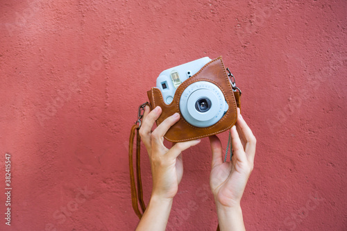 Woman hands holding a blue instax camera with a red wall on the background.
